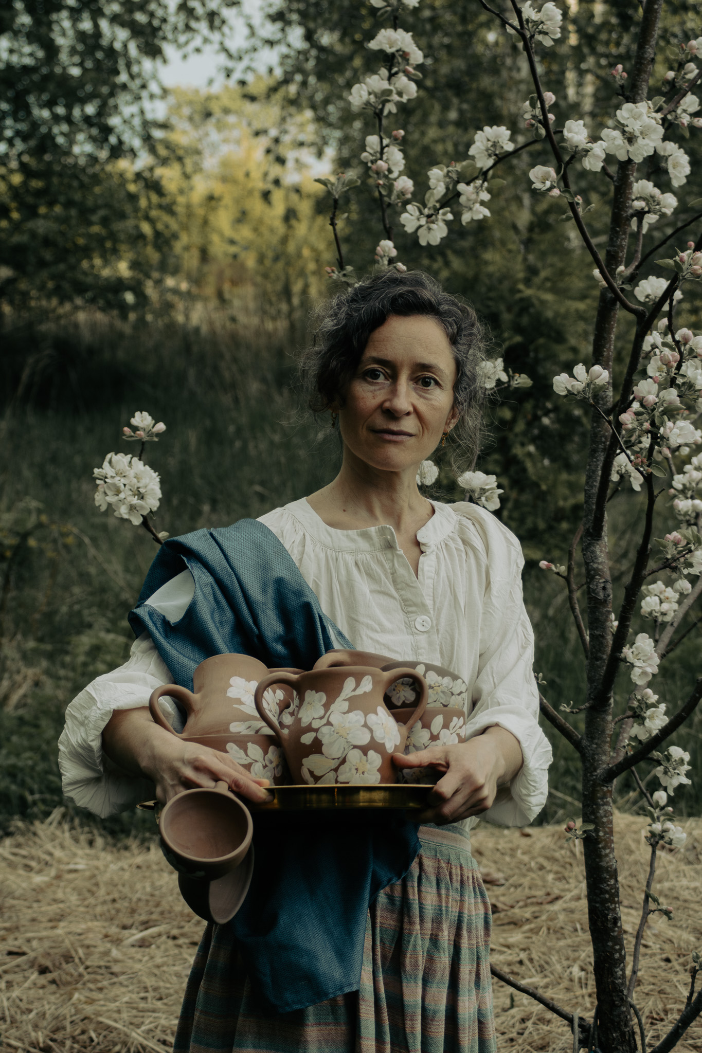 Victoria holding two dark handmade ceramic vessels in a summer field