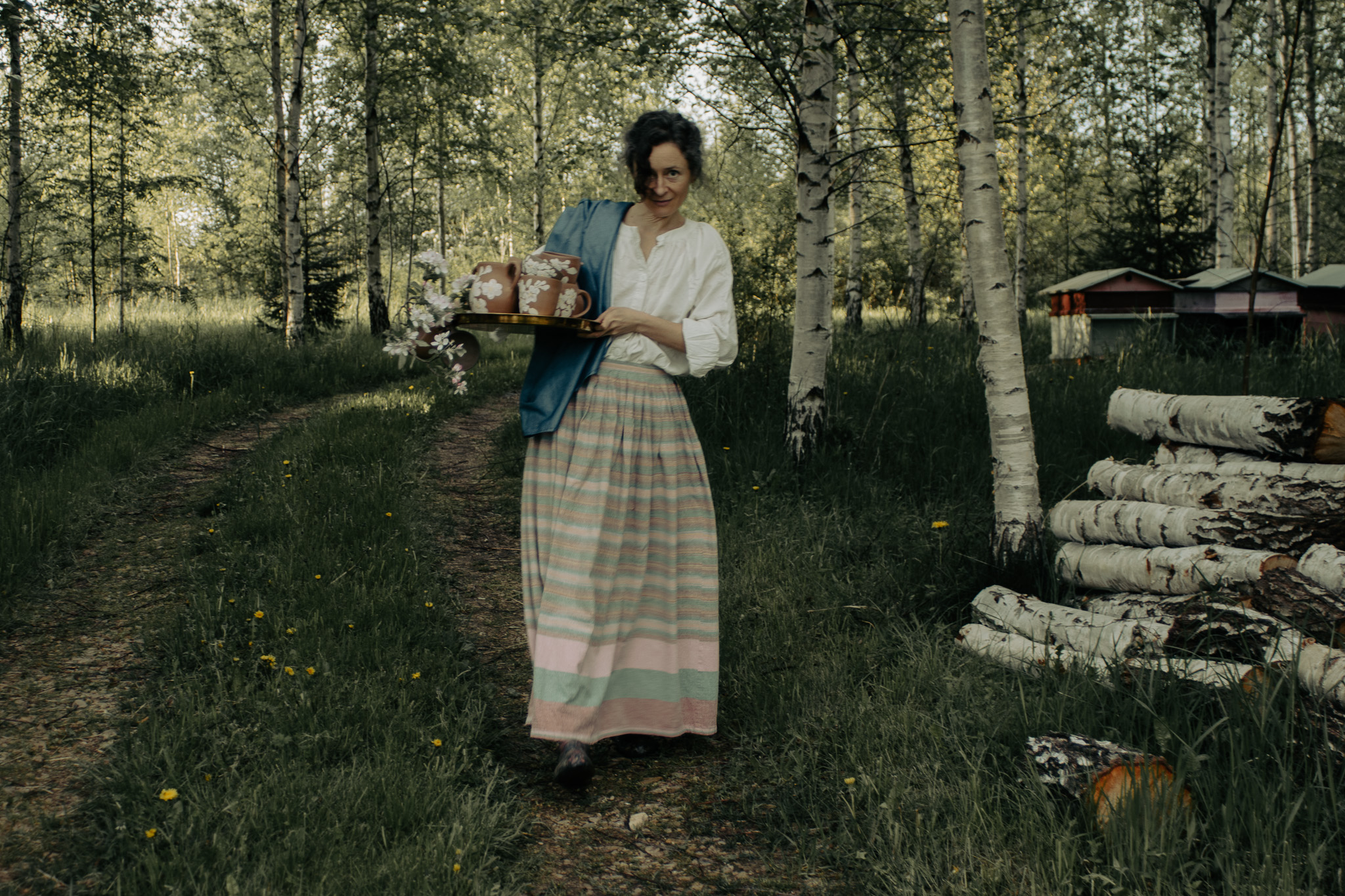 Victoria carrying handmade cups through a birch grove
