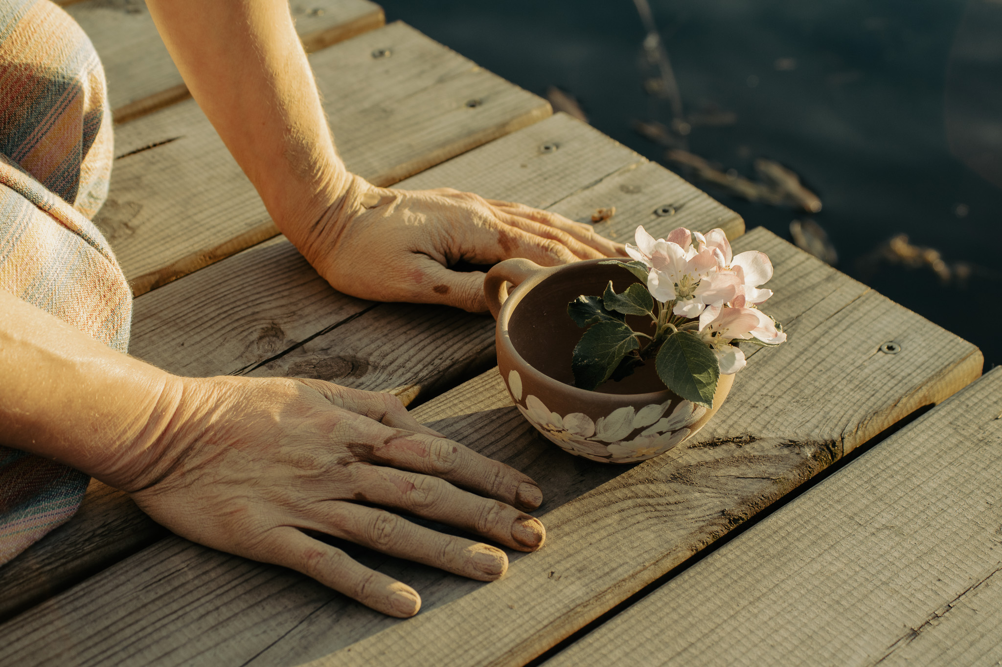 Clay-covered hands holding a small flowering branch